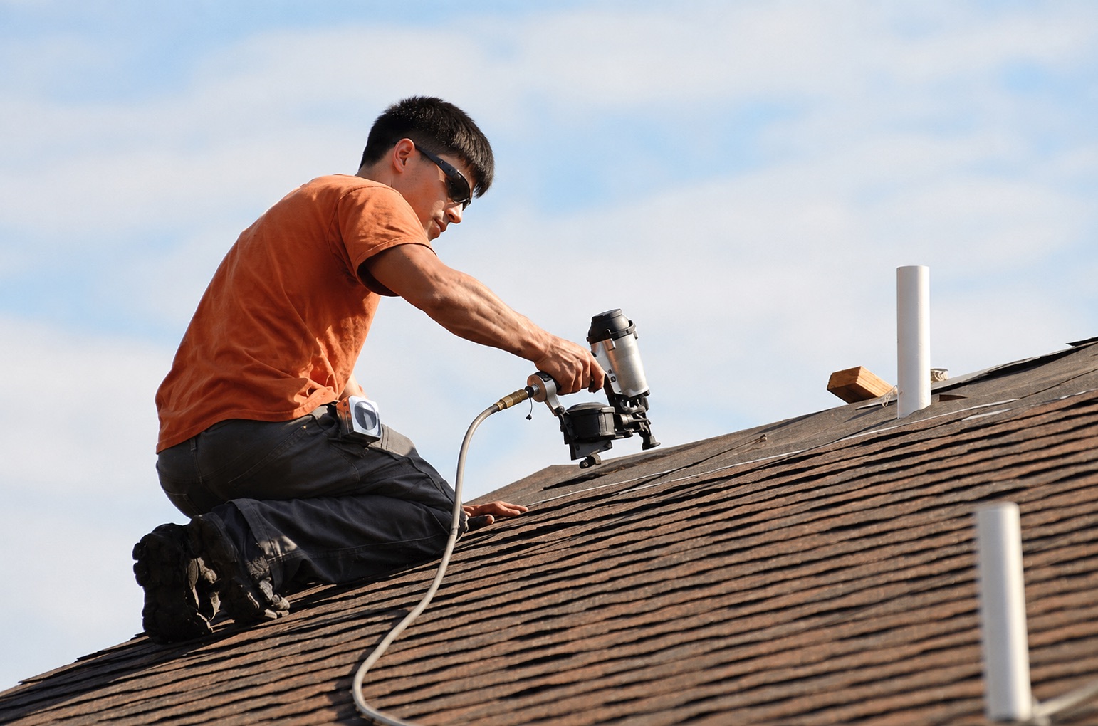 Roofer installing shingles with a nail gun on a residential roof